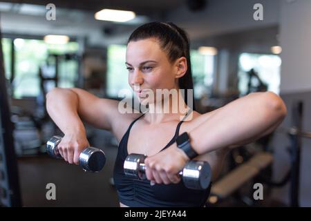 Junge kaukasische Frau hält Hanteln im Fitnessstudio Porträt Stockfoto