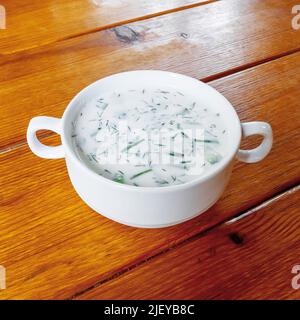 Eine weiße Keramikschale mit frischer Okroshka steht auf einem Holztisch. Leichte Sommerspeisen. Saisonales Gericht. Stockfoto