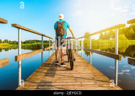 Rückansicht eines nicht erkennbaren Mannes mit Fahrrad auf einer Holzbrücke an einem sonnigen Tag. Konzept für einen aktiven Urlaub. Stockfoto