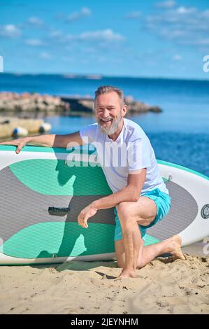 Mann auf dem Knie, der das Ruderbrett berührt und die Kamera anschaut Stockfoto