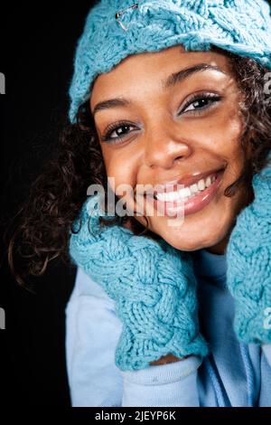 Hut und Handschuhe: Ein warmes Lächeln. Eine natürliche Schönheit mit freundlichem Gesicht, die sich in passendem Hut und Handschuhen warm hält. Teil einer Serie von Bildern mit demselben Modell. Stockfoto