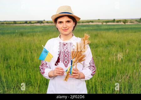 Unschärfe junge Frau in vyshywanka und Hut hält Bouquet von reifen goldenen Dornen von Weizen gebunden und Flagge auf der Wiese Natur Hintergrund. Flagge Ukrain Stockfoto