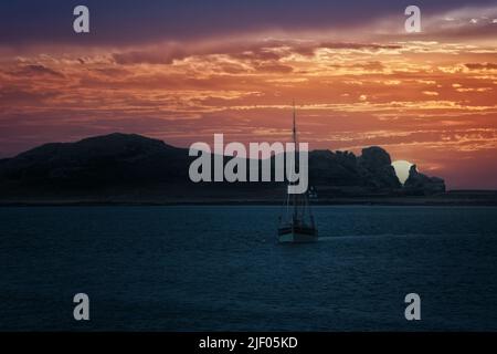 Segelboot an der Dublin Bay mit farbenprächtiger Himmel und untergehenden Sonnenstrahlen über Irlands Eye, einer kleinen unbewohnten Insel. Stockfoto