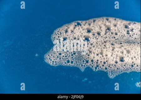 Seifenschaum vor farbigem Hintergrund. Blasen weißen Waschmittelschaums auf der blauen Oberfläche. Shampoo-Schaum-Textur. Selektiver Fokus. Stockfoto