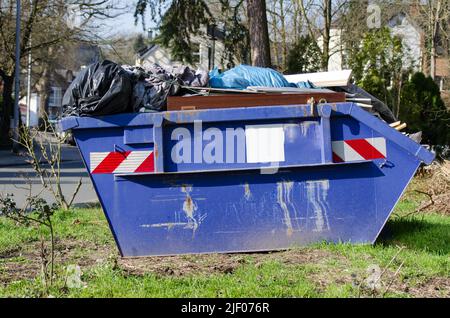 Blauer Behälter oder Müllcontainer mit sperrigem Abfall, der auf einem Rasen in einem Wohngebiet steht Stockfoto