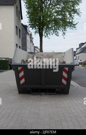 Grauer Behälter oder Müllcontainer mit Bauschutt oder Bauabfall. Container wird auf dem Bürgersteig in einem Wohngebiet platziert. Stockfoto