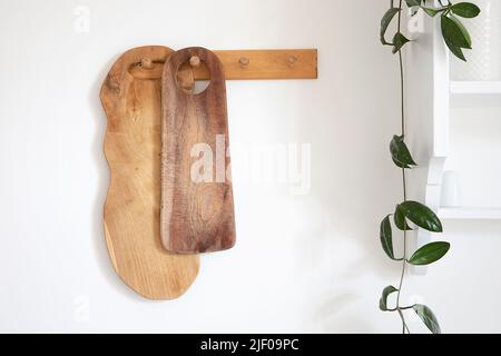 An der Wand hängt eine Holzschneidebrett-Kollektion. Gemütliche rustikale Stil moderne Küche Interieur Detail, grüne Pflanze und weißes Regal. Dekoration in Traditi Stockfoto