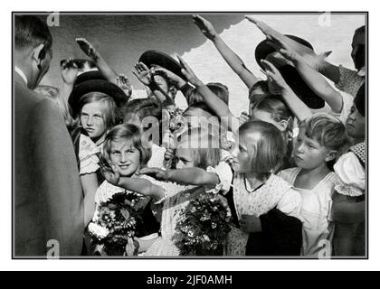 Adolf Hitler 1930er mit einer Gruppe glücklicher junger blonder arier Mädchen und Jungen Kinder mit Blumen, die ihn mit dem Nazi Heil Hitler Salut begrüßen. Nazideutschland 1936 Stockfoto