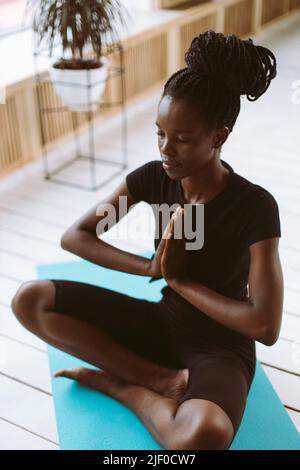 Vertikal meditierende, spirituelle multirassische Frau mit Händen in namaste Asana-Pose, sitzen in Yoga Lotus Grußhaltung Stockfoto