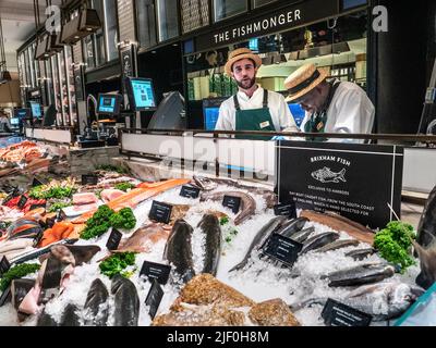 Harrods Fishmonger Fresh Brixham Fish Food Hall Interieur mit der Ausstellung „The Fishmonger“ mit einer großen Auswahl an exklusivem, handverlesenen Brixham UK Britischen Fisch im Tagesboot. Meeresfrüchte-Krustentiere zum Verkauf. Verkaufsassistenten tragen traditionelle Strohboater Hüte, Vorbereitung einer Kundenauswahl, Harrods Food Hall Fishmonger Department Store Mall Shop, Brompton Rd, Knightsbridge, London SW1X 7XL Stockfoto