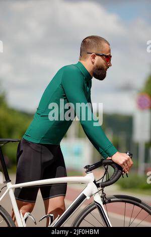 Porträt eines sportlichen Mannes in einem Radsport-Outfit, der mit einem Fahrrad auf der Bike Lane steht und für die Kamera posiert Stockfoto