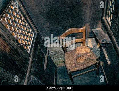 Beichtstuhl-Box-Kirche Rustikale Beichtstuhl-Box Innenansicht des kleinen Korbsessels des Priesters in einem einfachen strengen Beichtstuhl aus Holz in einer traditionellen römisch-katholischen Kirche Stockfoto