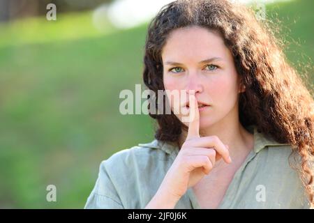 Seriöse Frau, die mit dem Finger auf den Lippen im Park um Ruhe bittet Stockfoto