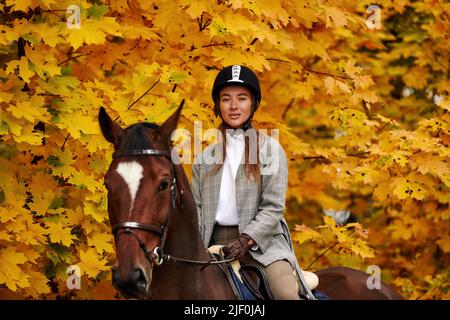 Junge schöne Brünette Mädchen reitet ein Pferd an einem warmen und sonnigen Herbsttag. Porträt einer hübschen jungen Frau auf dem Pferd, trägt hohe Stiefel und Stockfoto