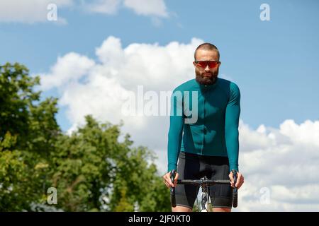 Porträt eines sportlichen Mannes in einem Radsport-Outfit, der mit einem Fahrrad auf der Bike Lane steht und für die Kamera posiert Stockfoto