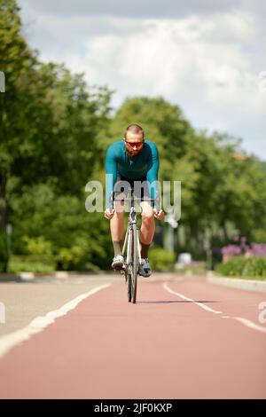 Porträt eines sportlichen Mannes in einem Radsport-Outfit, der mit einem Fahrrad auf der Bike Lane steht und für die Kamera posiert Stockfoto