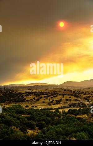 Riesige Wolke von rötlichen Rauch über den Bergen von einem Waldbrand und die Sonne, die durch die Wolken des Rauchs guckt. Madrid Spanien. Stockfoto