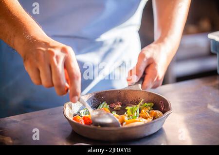 Gourmet-Koch in Uniform Zubereitung Mahlzeit, rührt mit Löffel Gemüse in der Bratpfanne Stockfoto