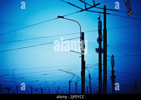 Straßenlampen, die durch Kabel verbunden sind, stehen in der Dämmerung der Nachtstadt am blauen Himmel. Elektrifizierung. Landschaft. Stockfoto