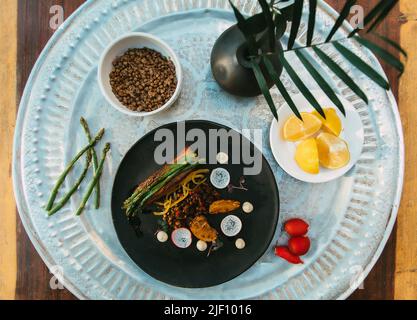 Vegetarische Gerichte im orientalischen Stil, die auf kleinen schwarzen und weißen Tellern mit grüner Pflanze und Bio-Gemüse auf einem Holztisch zubereitet werden Stockfoto
