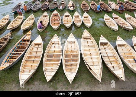 Manikganj, Dhaka, Bangladesch. 28.. Juni 2022. Hunderte von handgefertigten Holzbooten stehen auf dem größten Bootsmarkt von Bangladesch in Manikgonj, Bangladesch, zum Verkauf. Die Menschen strömten auf den Freiluftmarkt, um Boote zu kaufen, um sich auf die kommende Regenzeit vorzubereiten. Bangladesch, bekannt als „Ground Zero for Climate change“, ist mit zusätzlichem Stress konfrontiert, da fast 75 % von Bangladesch unter dem Meeresspiegel liegen und jährlich mit Überschwemmungen konfrontiert sind. Wird von den Einheimischen während des Monsuns verwendet, wenn starke Regenfälle das Flussufer zum Platzen bringen und nahe gelegene Städte und Dörfer untertauchen, kostet jedes Schiff zwischen Â£30 und Â£80 je nach Bedarf Stockfoto