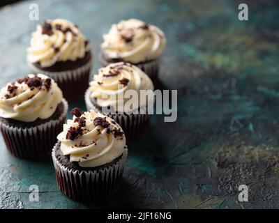 Schokoladen-Cupcakes mit Creme und geriebener Schokolade. Isoliert auf einem dunklen Hintergrund. Urlaub, Geburtstag. Auf dem Foto befinden sich keine Personen. Es ist kostenlos Stockfoto