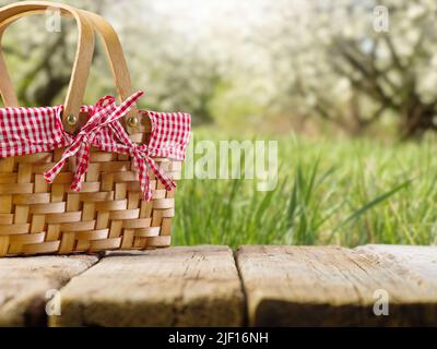 Sommerurlaub, Picknick. Auf einem Holztisch steht ein Strohkorb für ein Picknick vor dem Hintergrund einer malerischen Sommernatur. Feiertage mit freitag Stockfoto