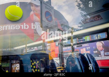 Im Fenster eines Busses spiegelt sich die britische Tennisspielerin Emma Raducanu am zweiten Wettkampftag während der Wimbledon Lawn Tennis Association Championships am 28.. Juni 2022 in London, England, auf einer riesigen Werbetafel im Stadtzentrum von Wimbledon wider. Stockfoto