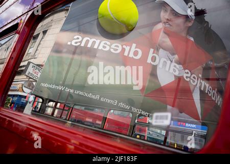 Im Fenster eines Busses spiegelt sich die britische Tennisspielerin Emma Raducanu am zweiten Wettkampftag während der Wimbledon Lawn Tennis Association Championships am 28.. Juni 2022 in London, England, auf einer riesigen Werbetafel im Stadtzentrum von Wimbledon wider. Stockfoto