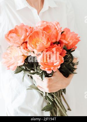 Junge Frau in weißen Kleidern hält ein großes Bouquet von korallenfarbenen Pfingstrosen. Vorderansicht Stockfoto