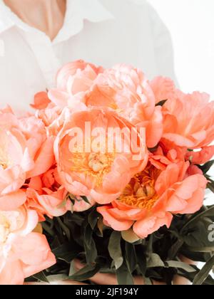 Junge Frau in weißen Kleidern hält ein großes Bouquet von korallenfarbenen Pfingstrosen. Vorderansicht Stockfoto