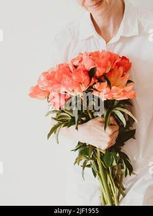 Junge Frau in weißen Kleidern hält ein großes Bouquet von korallenfarbenen Pfingstrosen. Vorderansicht Stockfoto