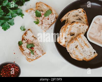Frisch hausgemachte Hähnchenleber-Pastete auf Toast hausgemachtes Brot mit Petersilie und Gewürzen auf dem Tisch. Draufsicht Stockfoto