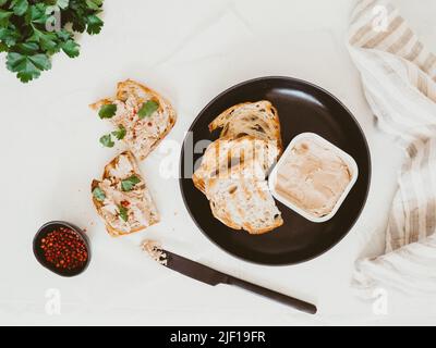 Frisch hausgemachte Hähnchenleber-Pastete auf Toast hausgemachtes Brot mit Petersilie und Gewürzen auf dem Tisch. Draufsicht Stockfoto