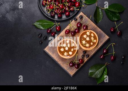 Köstlicher frischer Nougat und Nusstarte mit frischen Beeren auf einem Holzschneidebrett vor dunklem Beton Stockfoto