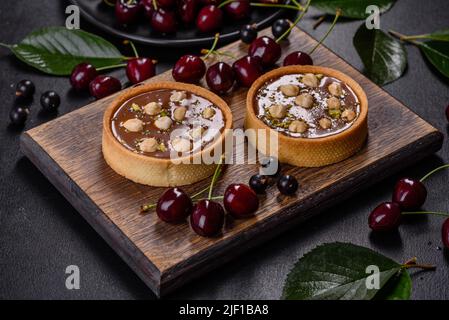 Köstlicher frischer Nougat und Nusstarte mit frischen Beeren auf einem Holzschneidebrett vor dunklem Beton Stockfoto