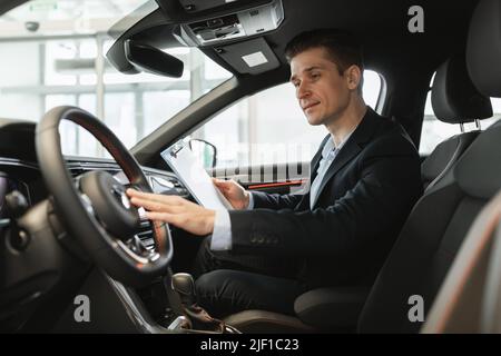 Glücklicher Versicherungsagent, der im neuen Auto sitzt und im Autohaus-Center eine Selbstuntersuchung macht, Leerraum Stockfoto