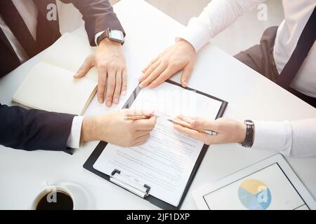 Nicht erkennbare Geschäftsleute in formeller Kleidung sitzen am Tisch und zeigen auf Papiere, während die Partnerschaft Vertrag bei der Sitzung zu diskutieren Stockfoto
