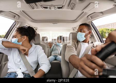 Kranke afrikanische Frau hustet mit Gesichtsmaske im Auto sitzen Stockfoto