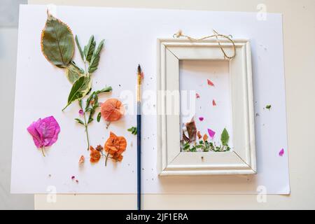 Blumenherbarium auf einem Blatt Papier. Blumen und Blätter auf einen Bilderrahmen gepresst, Pinsel und weißes Papier auf einem Tisch. Stockfoto