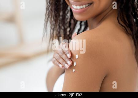 Die Haut Ist Murisierend. Lächelndes Schwarzes Weibchen, Das Nourishing Body Lotion, Closeup Shot, Anwendet Stockfoto