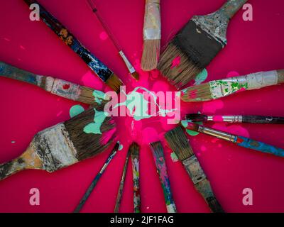 Horizontale Komposition, bei der einige alte und gebrauchte Pinsel verschiedener Größen auf einem magentafarbenen oder fuchsienfarbenen Hintergrund und mit rosa und hellgrüner Farbe erscheinen Stockfoto
