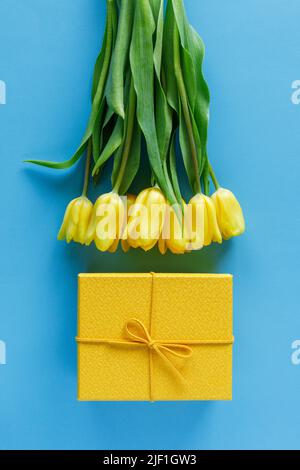 Gelbe Tulpen und Geschenkbox auf blauem Hintergrund. Blumenstrauß und auf farbigem Hintergrund Stockfoto