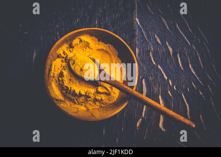 Indisches Kurkuma-Pulver, Kurkuma-Gewürz in kleiner Schüssel mit Löffel, Haldi-Pulver auf Holzhintergrund Stockfoto