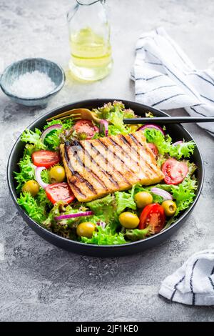 Frischer Salat mit gegrilltem Käse, Tomaten und Oliven auf grau Stockfoto