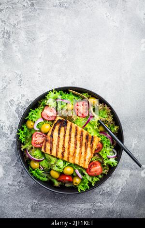 Frischer Salat mit gegrilltem Käse, Tomaten und Oliven auf grau Stockfoto