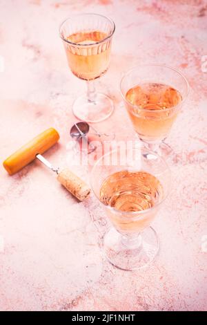 Drei Gläser Roséwein bei einer Weinprobe mit Flaschenöffner auf rosafarbenem Marmorhintergrund Stockfoto
