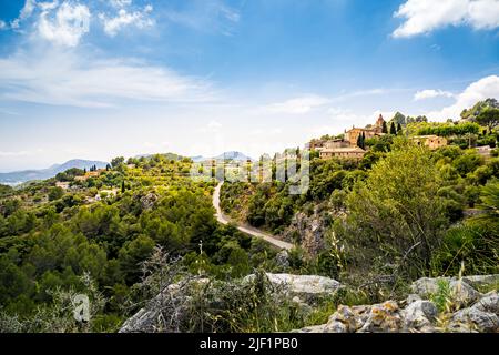 Blick von einem Felsblock über das Bergdorf Galilea auf Mallorca in der Gemeinde Puigpunyent, umgeben von Bergen und mediterranem Wald. Stockfoto