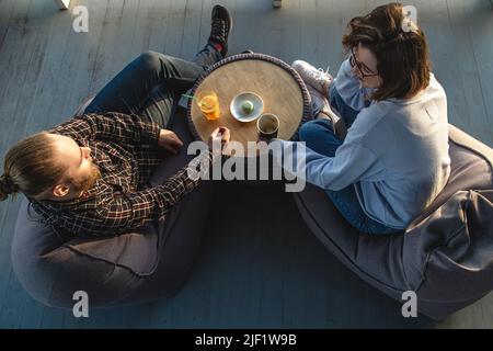 Eine junge Frau und ein Mann sprechen, während sie auf Sitzsäcken sitzen, Draufsicht. Stockfoto