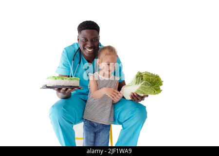 Ein afroamerikanischer Arzt erzählt einem kleinen Kind von gesunder und richtiger Ernährung, während er einen Kuchen und Kohl in der Hand hält. Das Konzept der Gesundheit Stockfoto